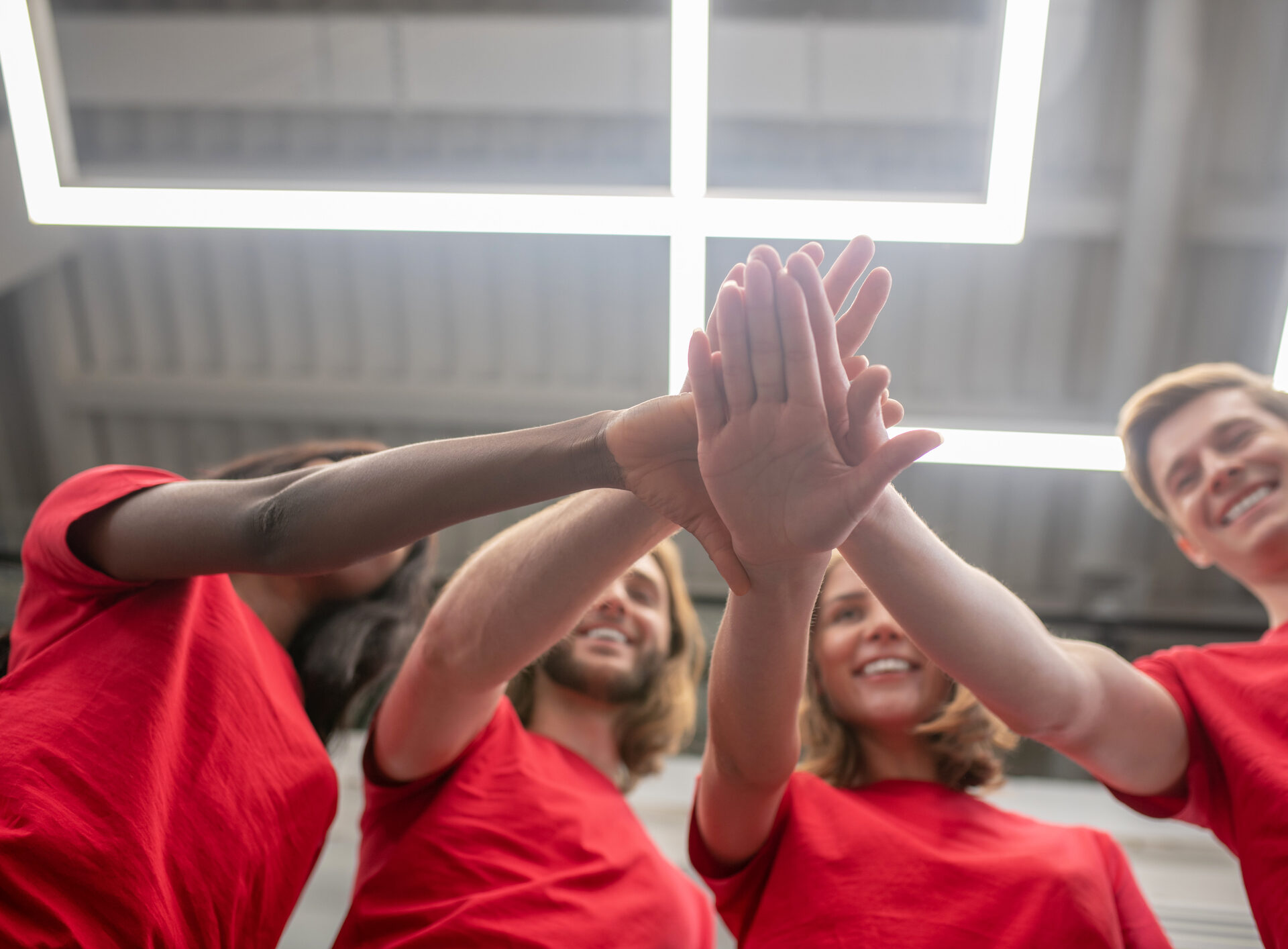 Four people with red shirts with their hands together in front of the camera - alumni volunteering