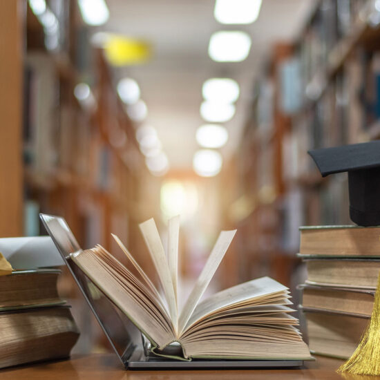 open book and cap and diploma with library shelf in background