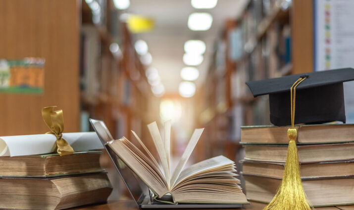 open book and cap and diploma with library shelf in background