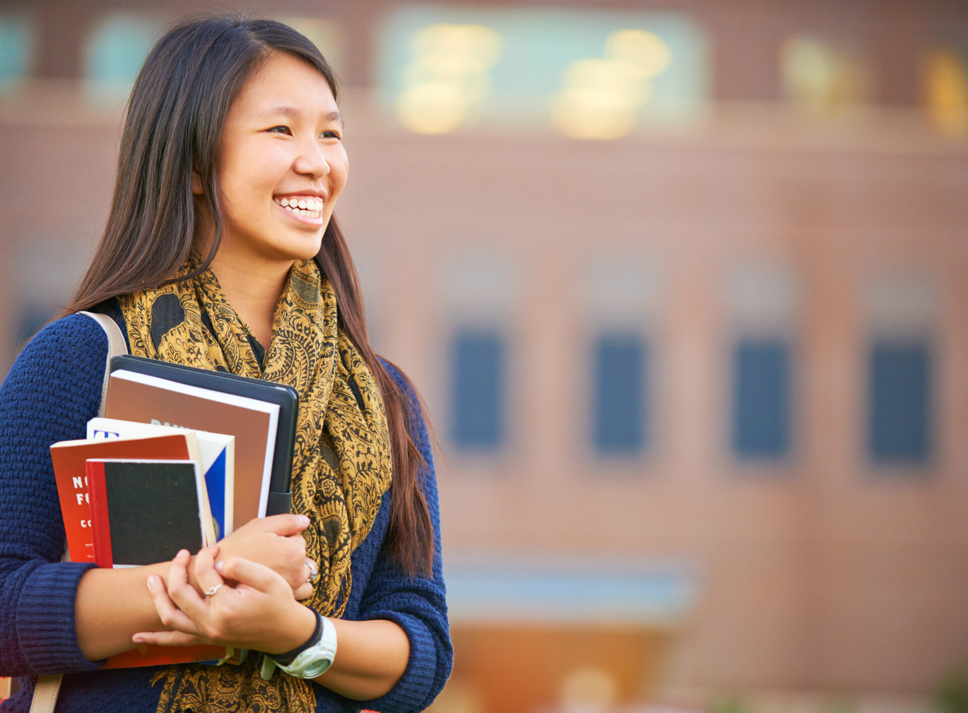 Shot of a young female student standing with her books on campus smiling and looking on; campus booksstore