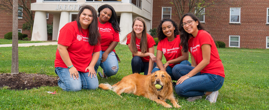 Res Life girls kneeling around dog with tennis ball in his mouth