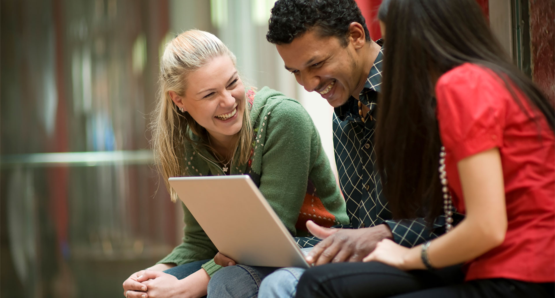 three adult students laughing while looking at laptop; Graduate + Doctoral Programs