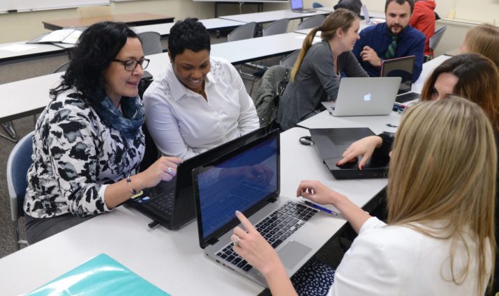 adult students interacting in a classroom, laptops
