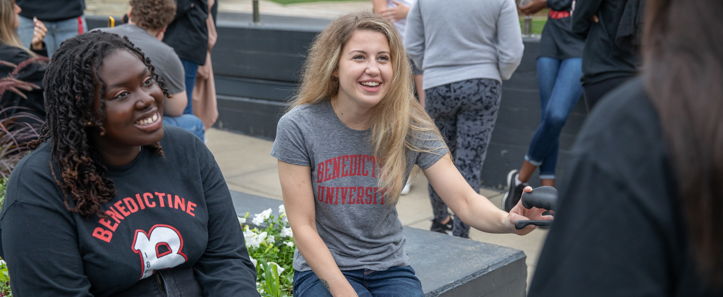 female students sitting outside with a group of students talking and laughing