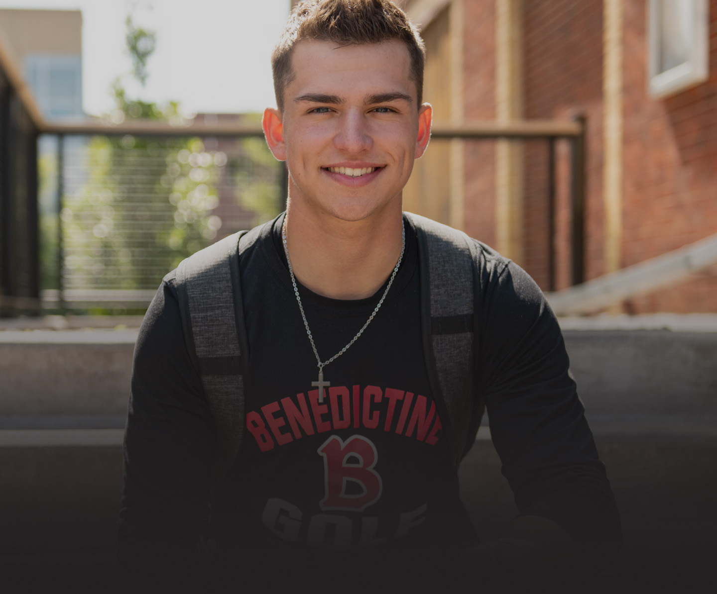 Male student in Benedictine t-shirt smiling on steps of Coal Ben