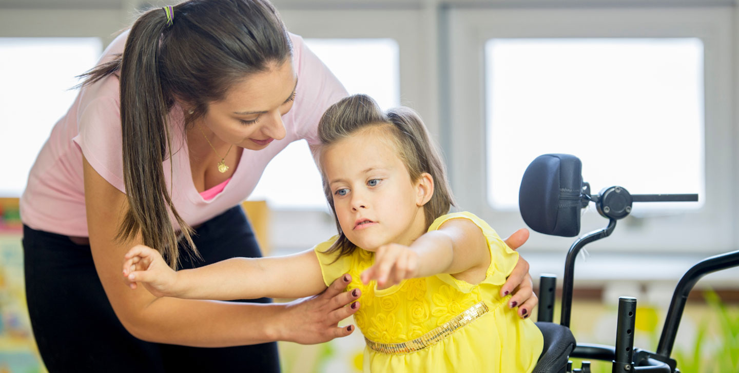 physical therapist helping a small child out of a wheelchair; pre-physical therapy