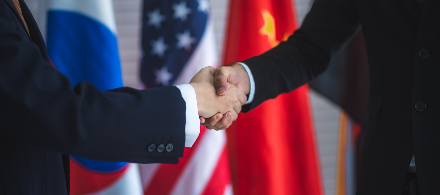 two hands shaking in front of multinational flags; international business and economics