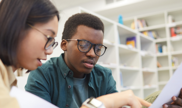 two student in library looking at a paper together