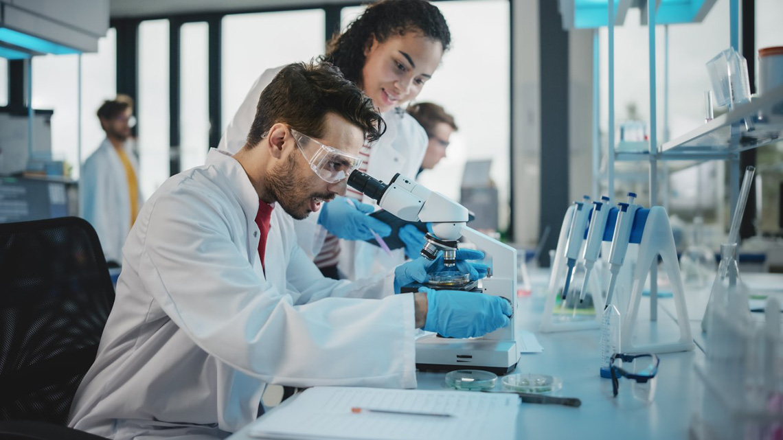 male student looking in microscope with female student watching