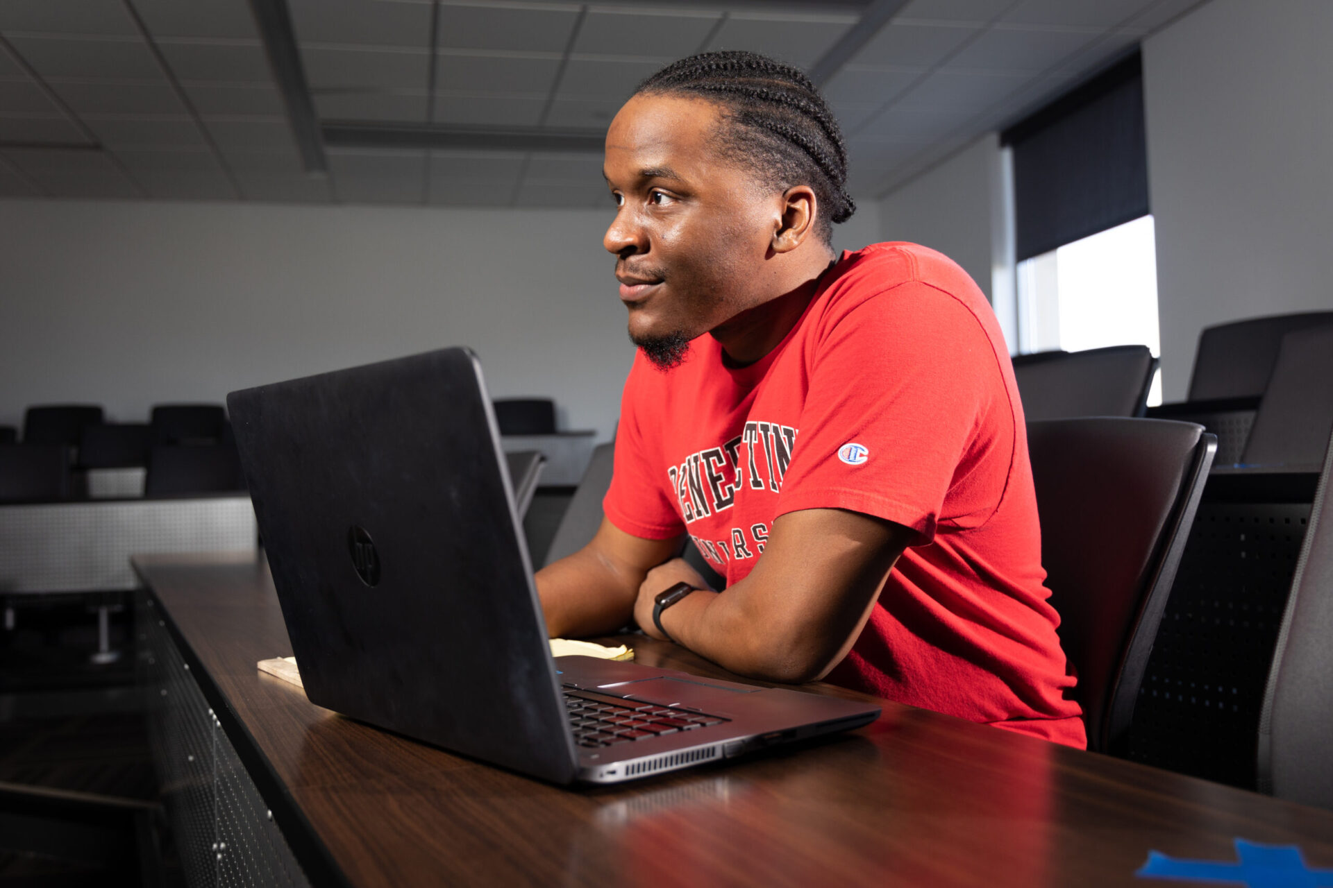 Male student in classroom with laptop and notes