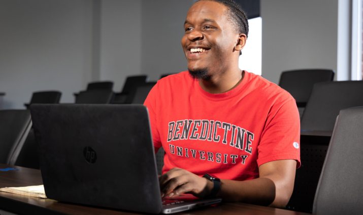 Male student in classroom with laptop and notes