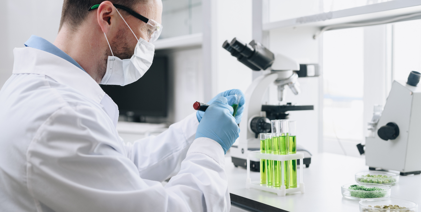 male student in lab coat and mask working with material in a test tube; molecular and cellular biology program