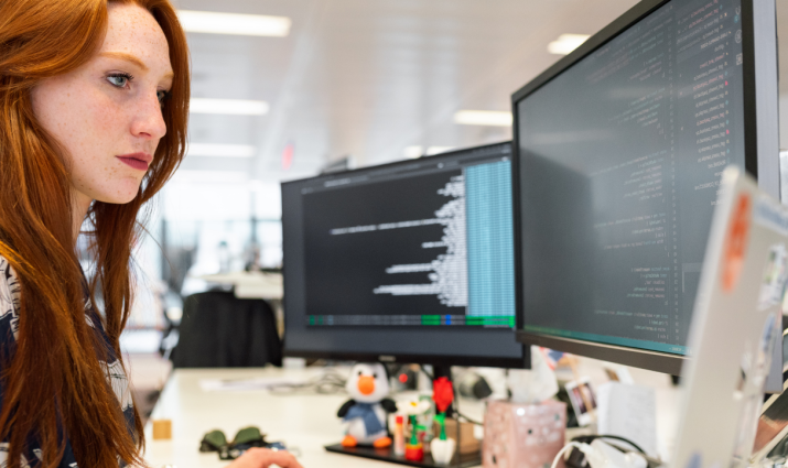 female student looking at two computer screens while working at her desk; computer science