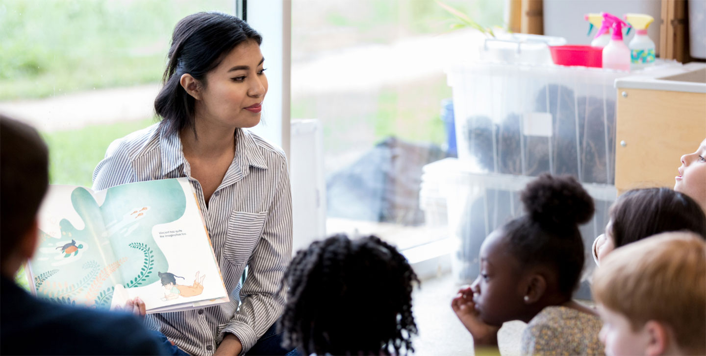 Asian teacher reading a book to a group of elementary education students