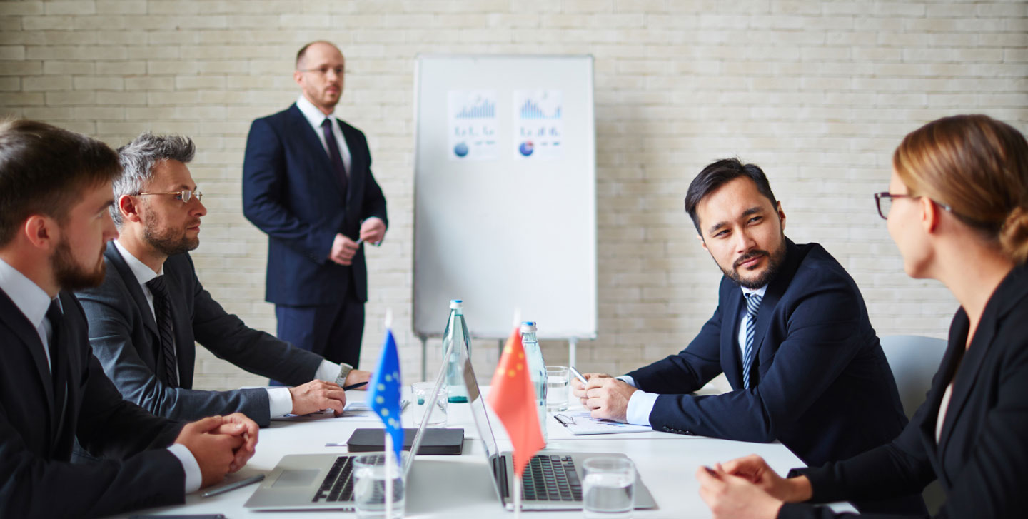 adult professionals at a conference table, one male in suit presenting to the others; global studies