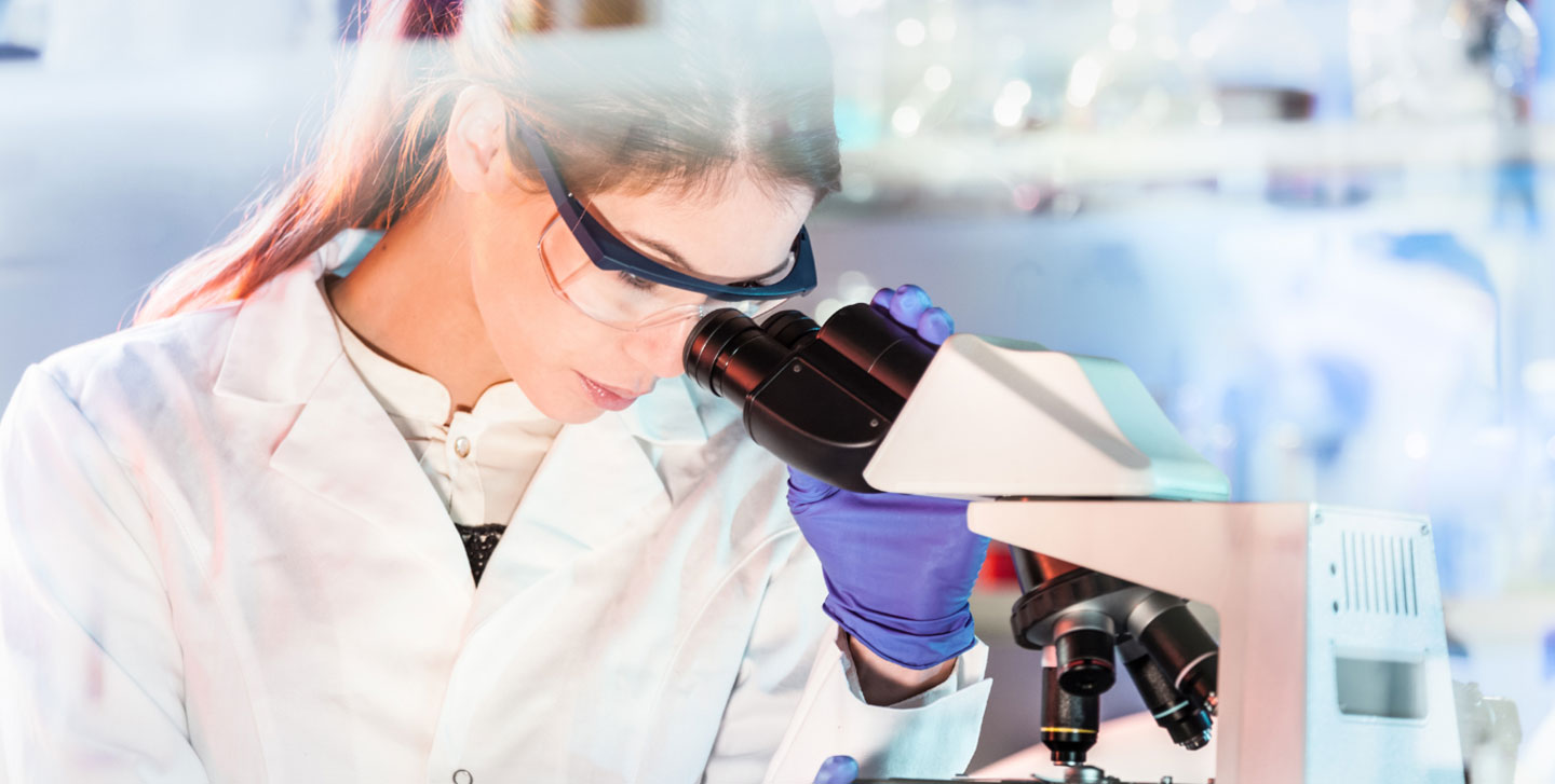 female student with lab coat looking through microscope; health science