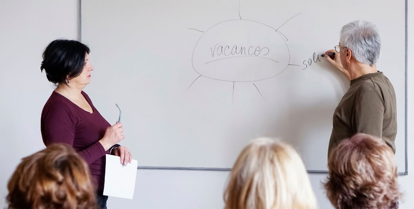 older student writing on white board while instructor looks on; linguistics