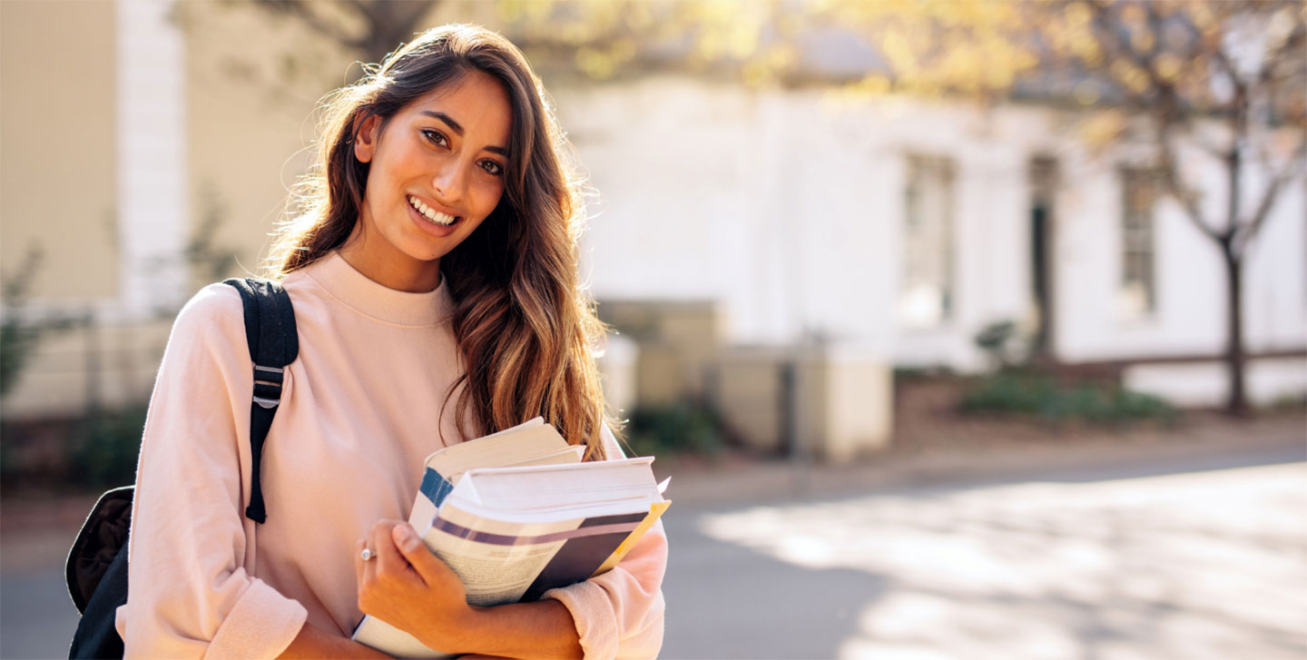 female student with backpack outside walking holding books