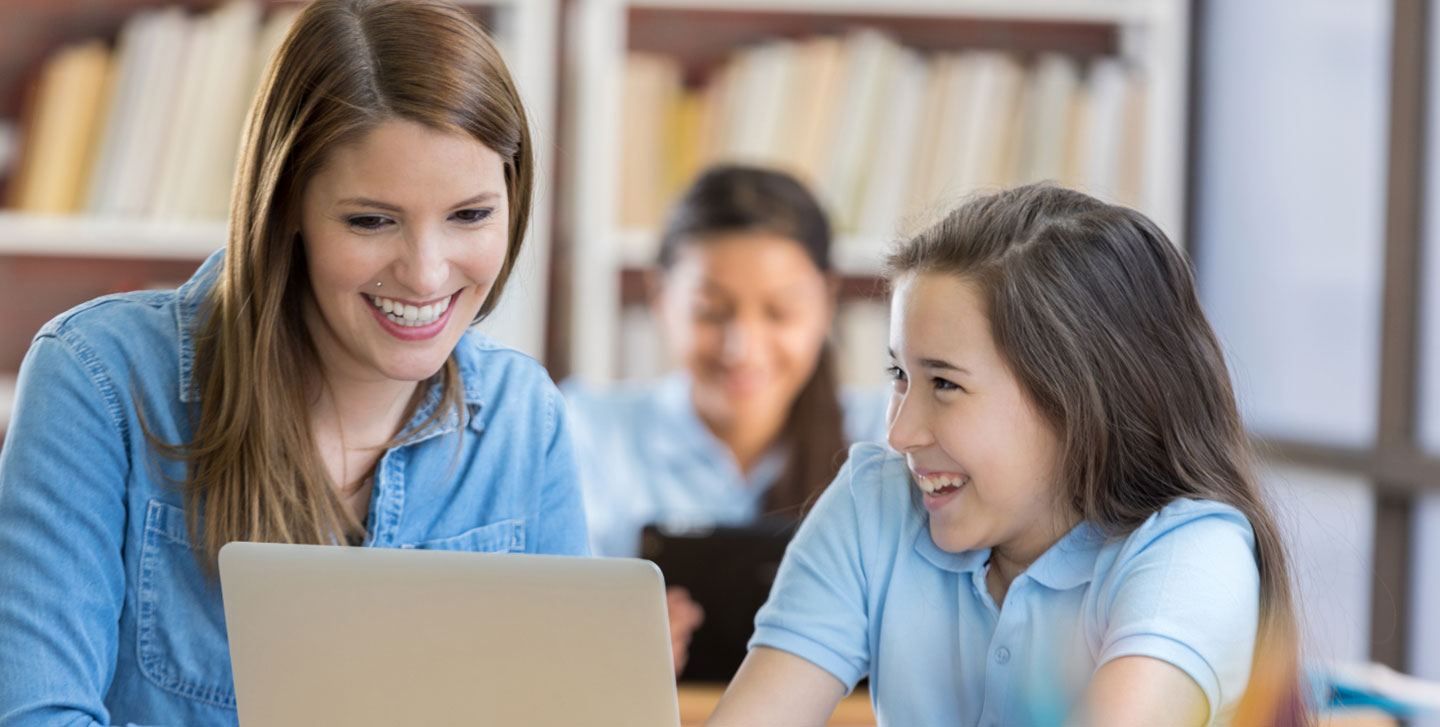 female student teacher working with middle school student on the computer