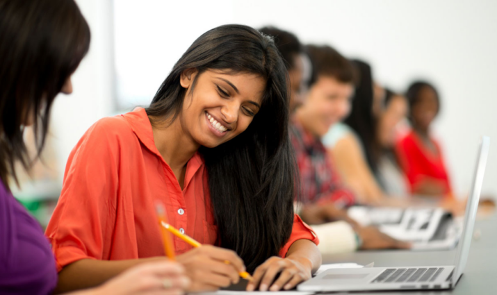 female student smiling while taking notes at her laptop; writing and publishing program