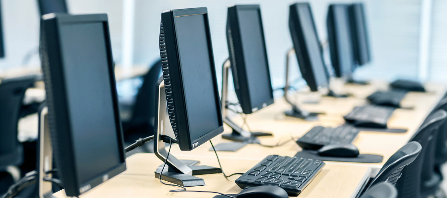 computer screens lined up on long desk in computer lab; computer information systems