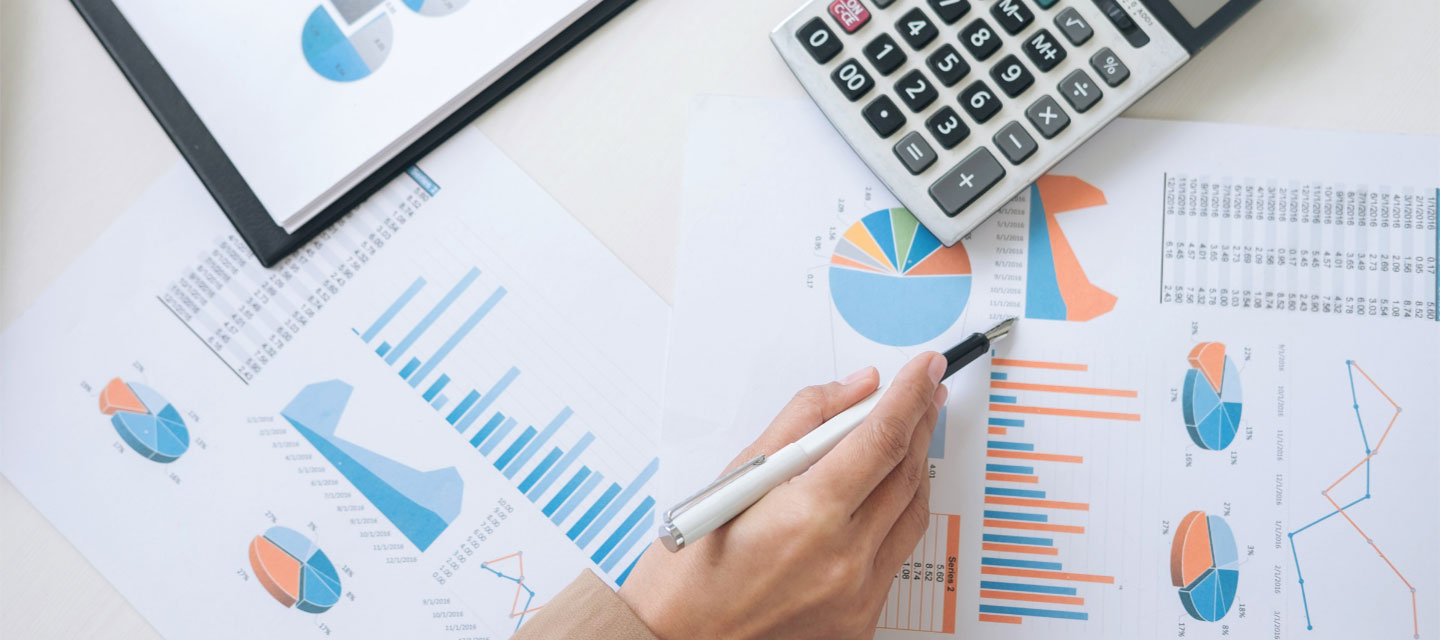 hand with pen pointing at graphs and charts laid out on a table; finance