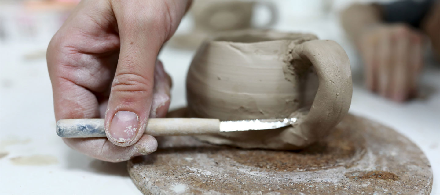 hand working with knife on a clay cup project; studio art
