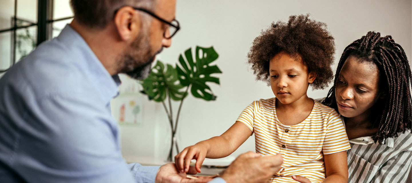 Male psychologist working with younger child who is sitting on her mother's lap; clinical psychology program