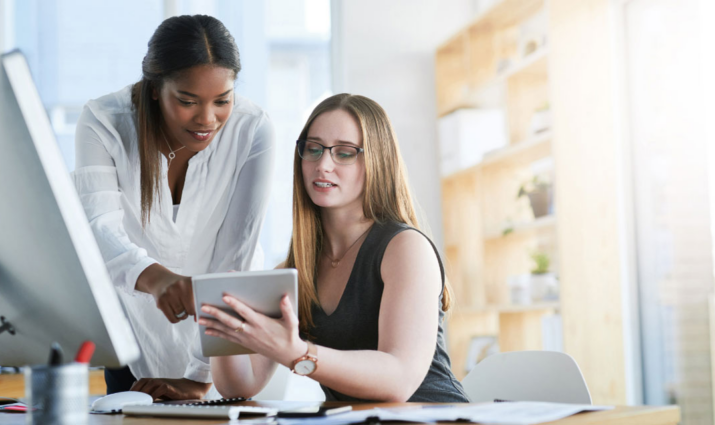 two female marketing professionals looking at a notebook discussing project; marketing