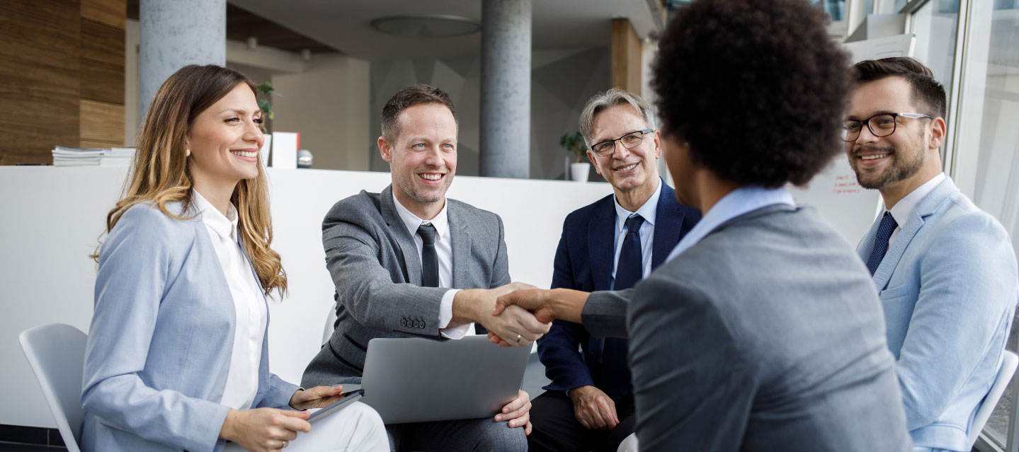 group of professionals sitting together, two are shaking hands; management and organizational behavior MS program