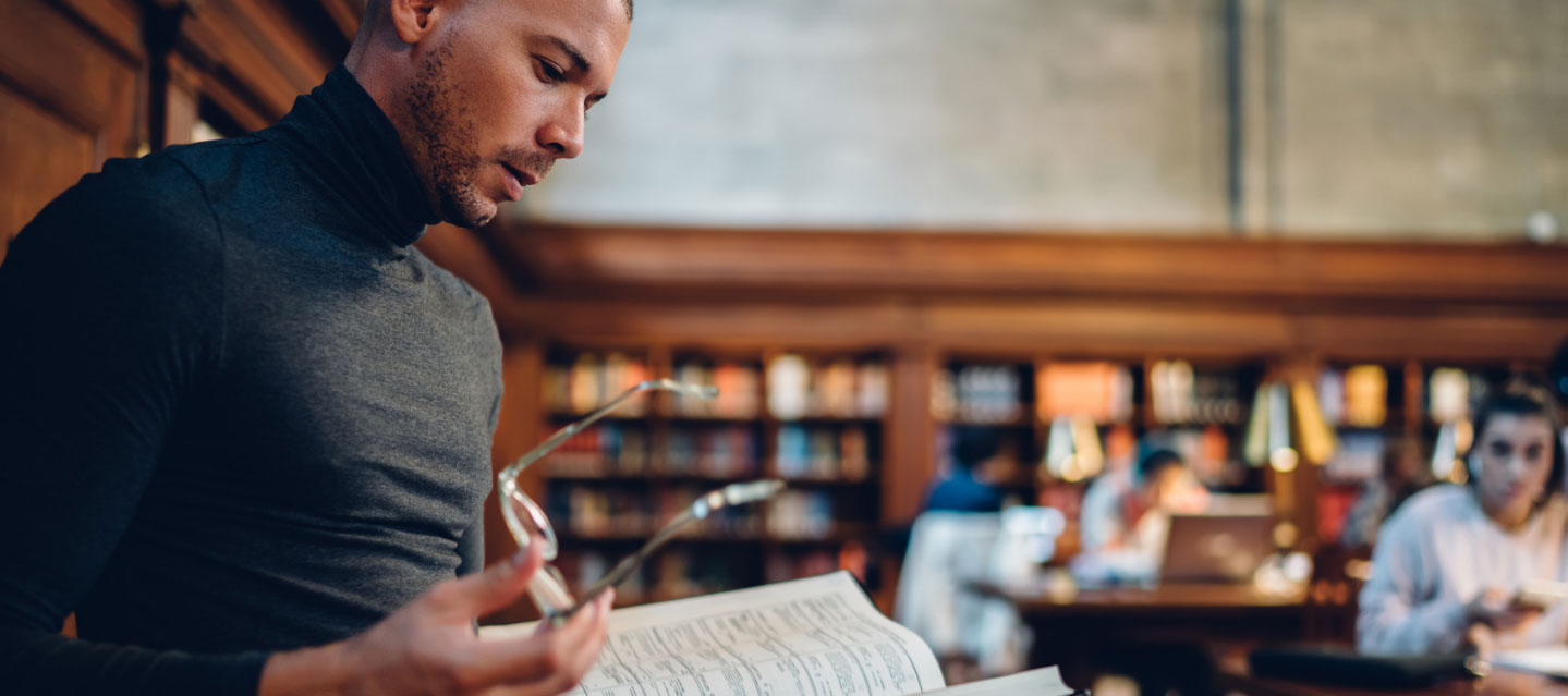 male instructor looking at book in the library; philosophy