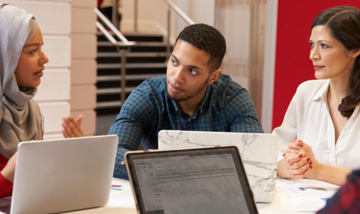 multi-racial students sitting at table with computers dialoging; theology