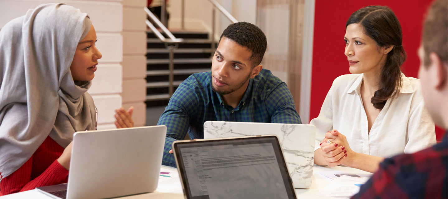 multi-racial students sitting at table with computers dialoging; theology