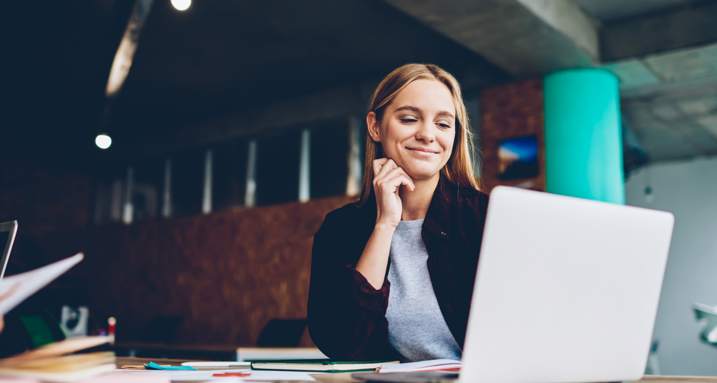 female professional looking at her laptop and smiling at her desk; communication arts