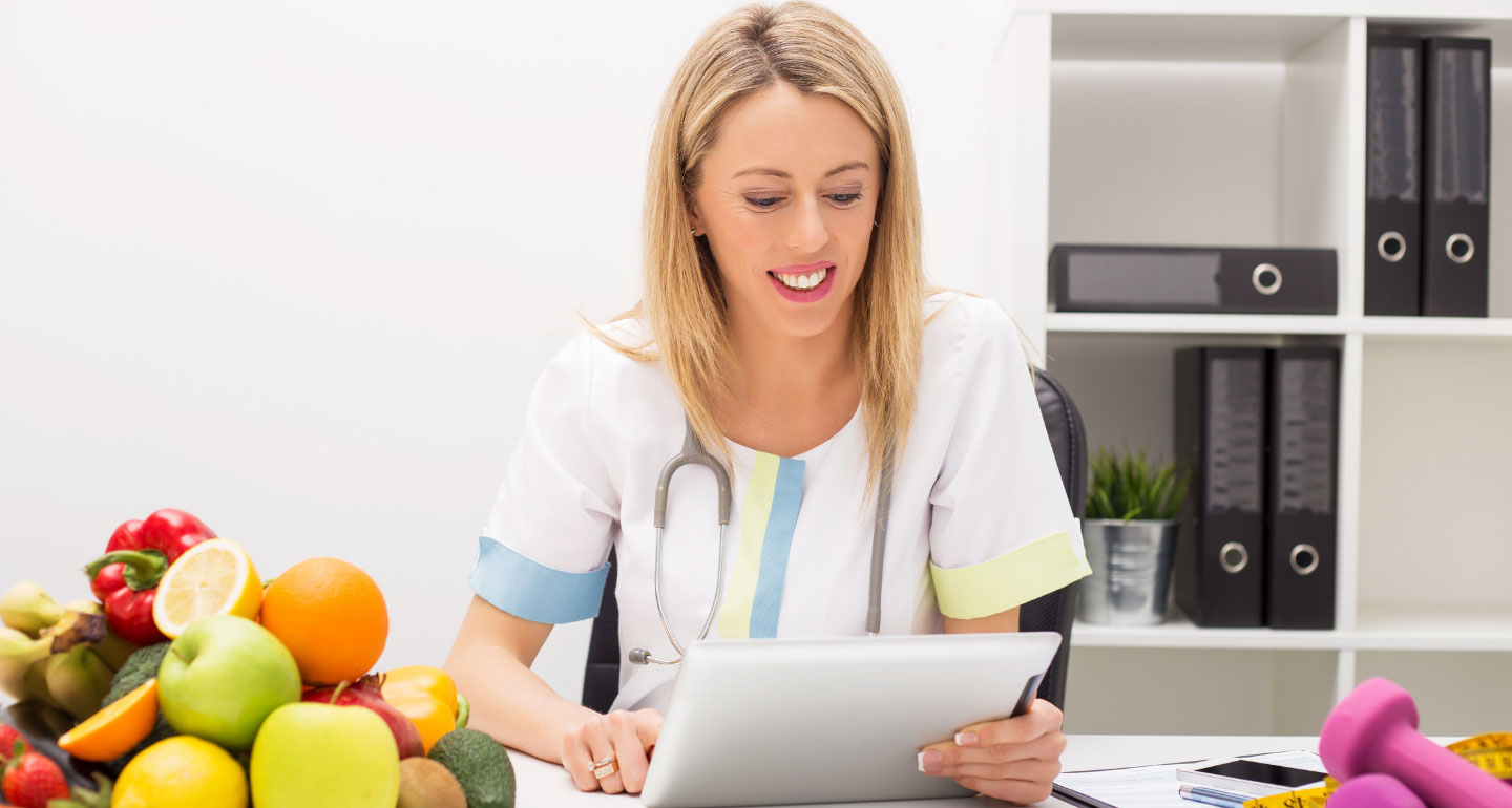 female dietician holding paperwork with bowl of fruit on the table with her; nutrition and wellness MS program