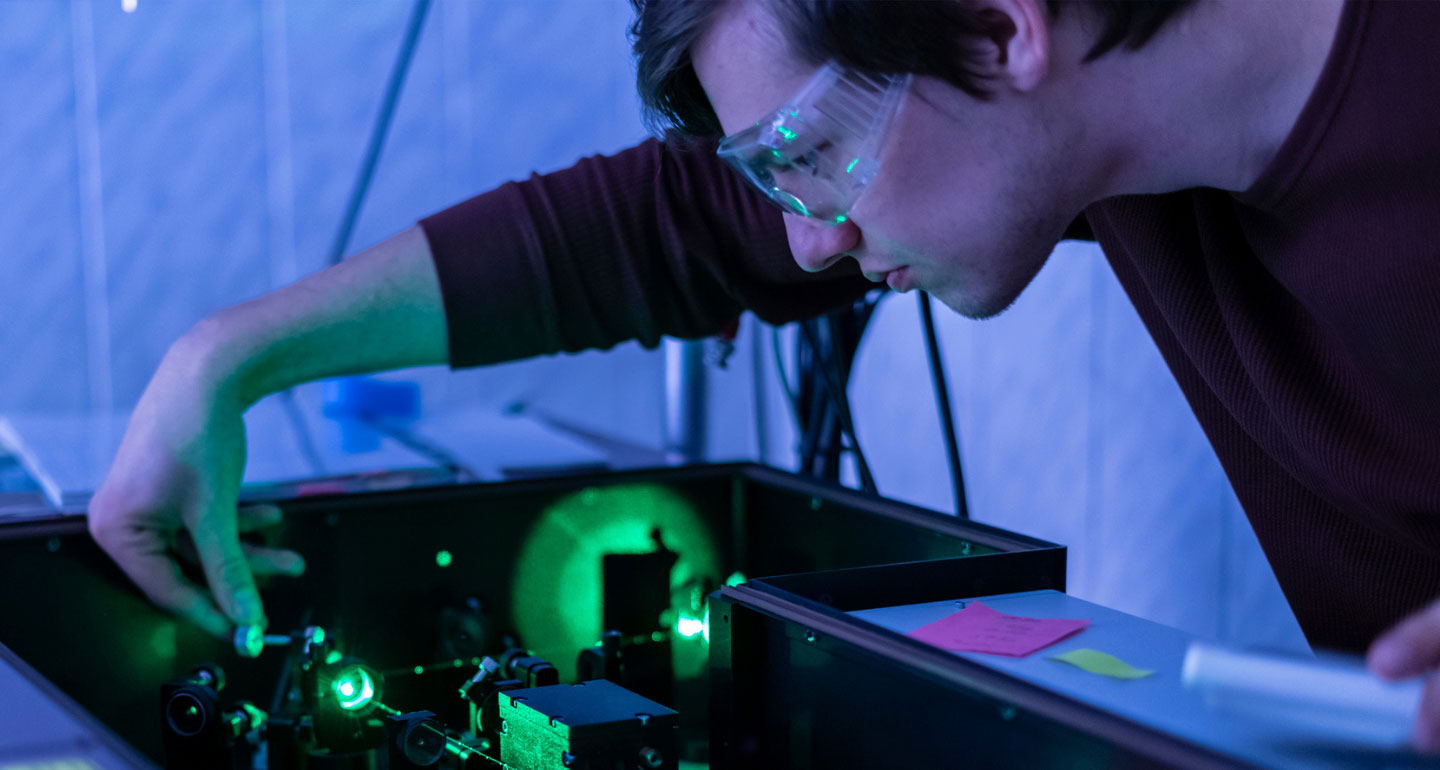 male student looking at lasers that are arranged on table; physics