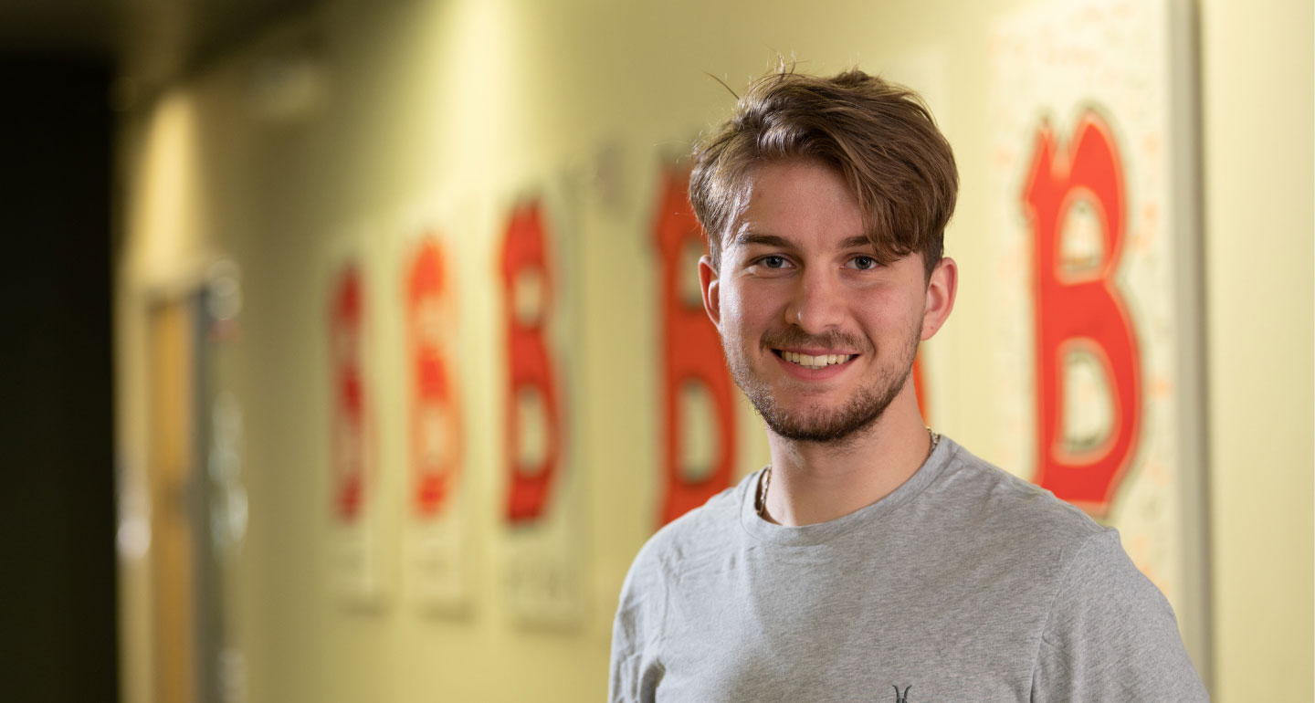 Headshot of male student smiling with Benedictine "B" logos on the wall behind him; special education