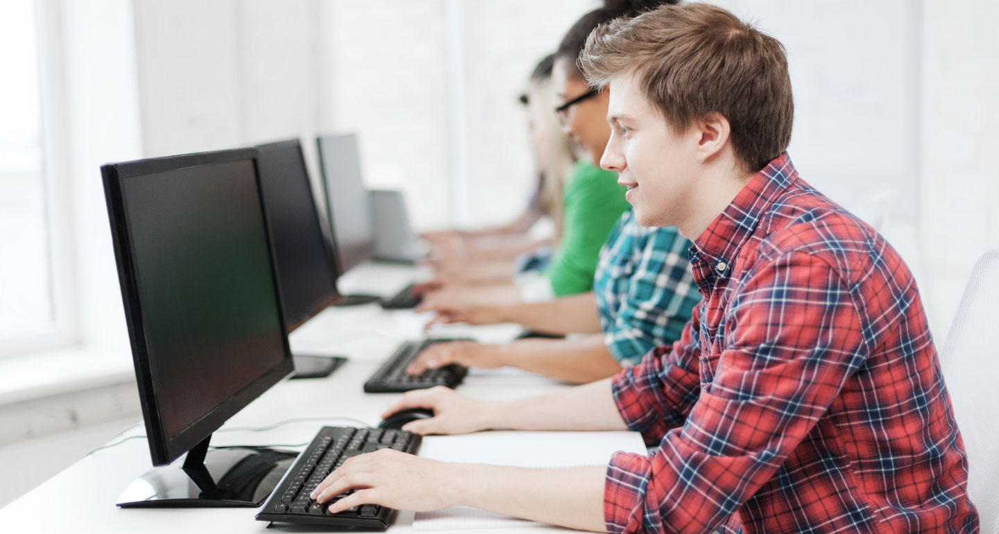 students in a row working on computers; first student is in focus, others are blurred; placement testing