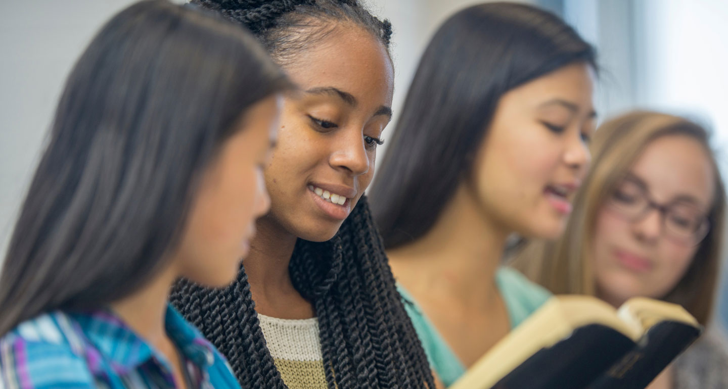 group of young women, one singing in the background while other look at book; Catholic high school award-Lisle