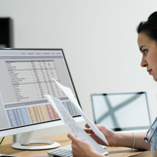 Nursing student looking at paperwork while in front of a computer screen; MSN/MBA program