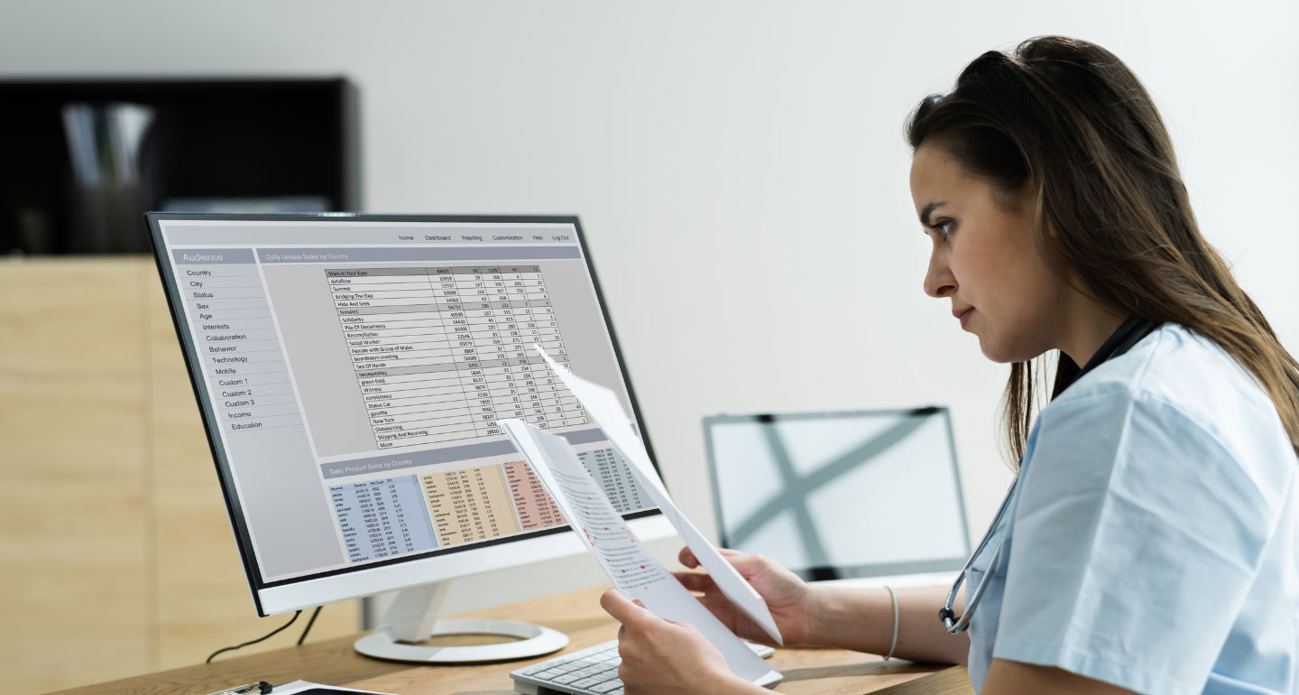 Nursing student looking at paperwork while in front of a computer screen; MSN/MBA program