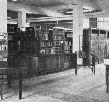 historic black and white photo of library book shelves and tables and chairs; archives