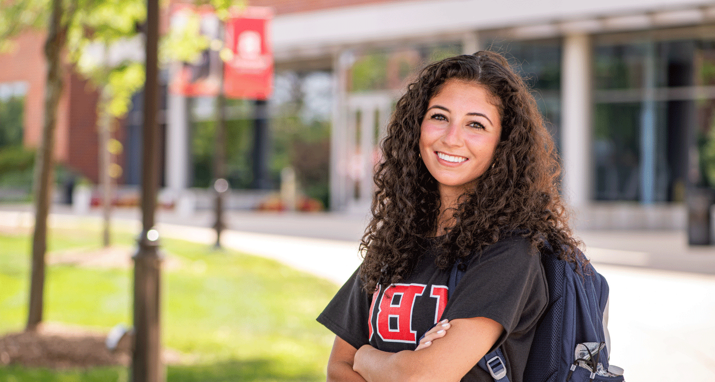 Close-up of female student in front of Goodwin Hall smiling with arms crossed; Financial Aid
