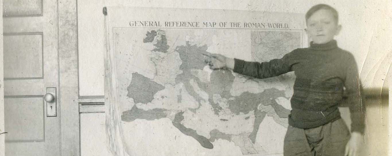 historic black and white photo of young boy pointing to map on the wall; student services
