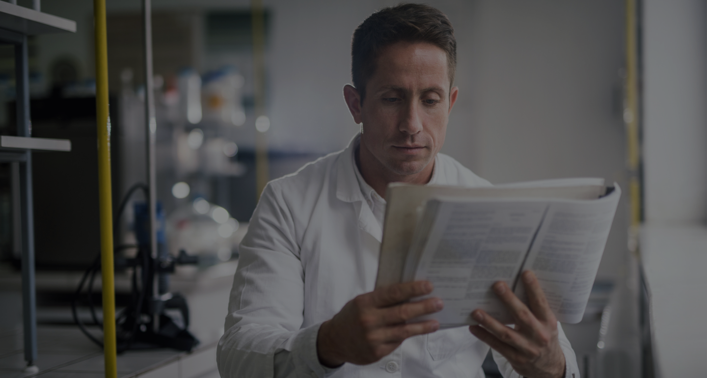 Male sitting reading a manual, image has a black overlay; Interlibrary Loan
