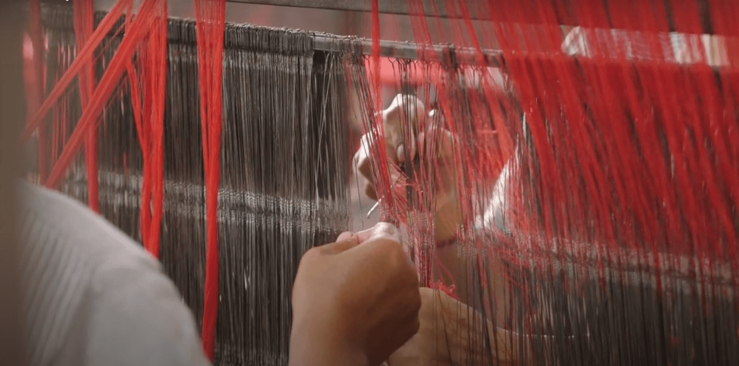 hands weaving red and gray threads hanging on a rod