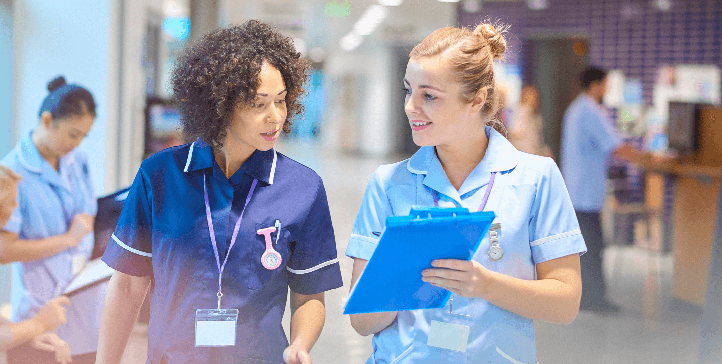 female nurses, one sharing clipboard with the other