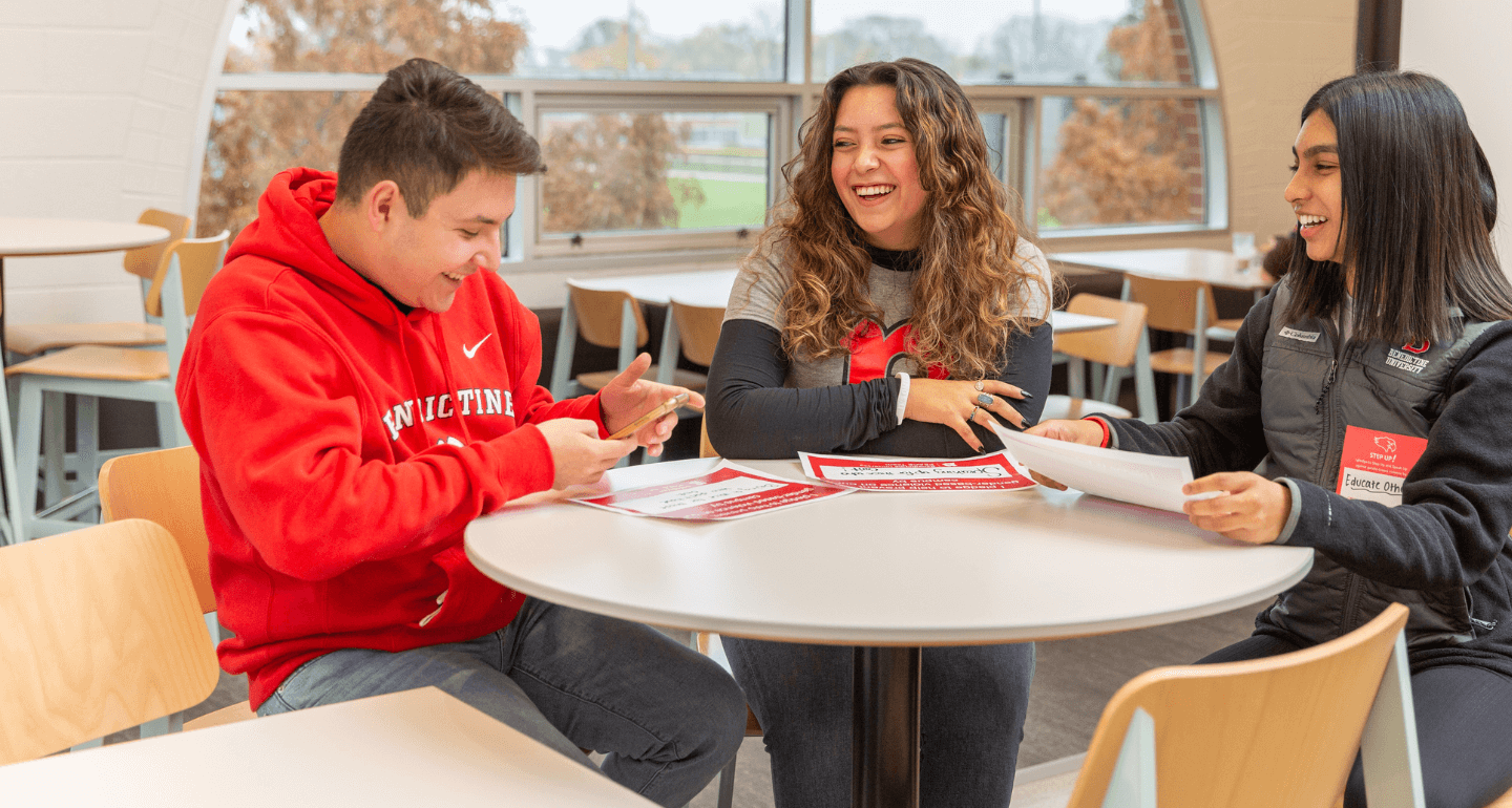 group of students in cafeteria laughing and looking at phone