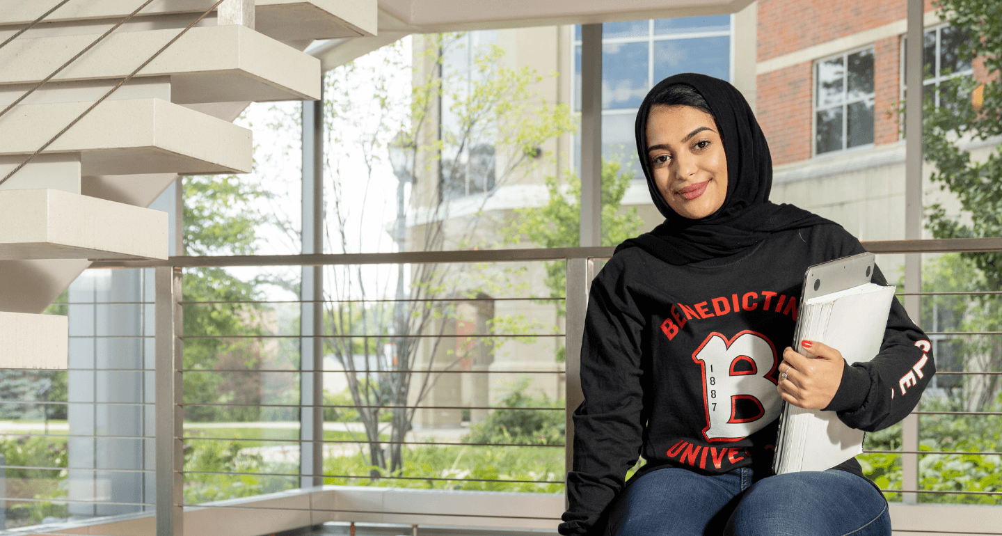 female student sitting on railing holding books in Goodwin Hall