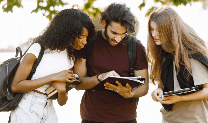 International transfer students looking at a notebook the middle student is holding